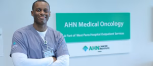 A man in medical wear stands in front of a Medical Oncology sign