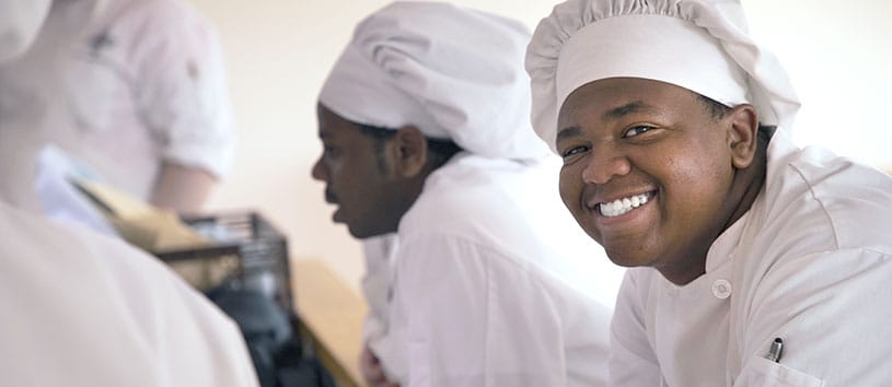 A culinary arts student stands in a food prep zone and smiles