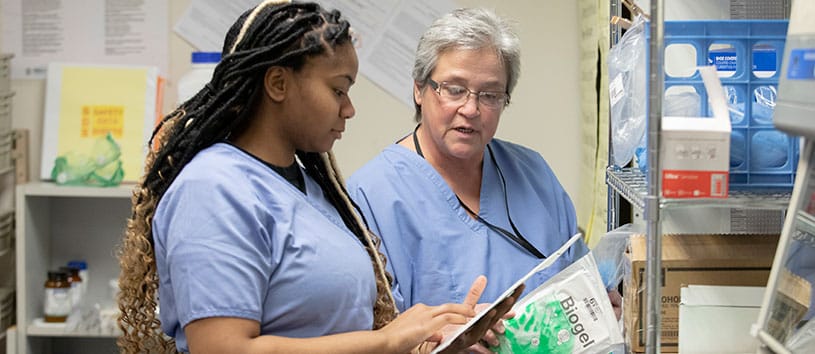 Two medical assistant students look at various medical products on a shelf 