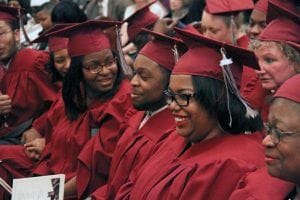 A row of graduates in caps and gowns sit at a graduation ceremony 